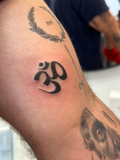 Verse zwarte Om-symbool tattoo op de bovenarm.