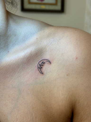 Minimalistische halve maan met takje en blaadjes op het sleutelbeen.