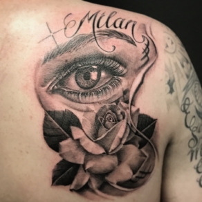 Realistisch oog met roos en naam 'Milan' op schouderblad.