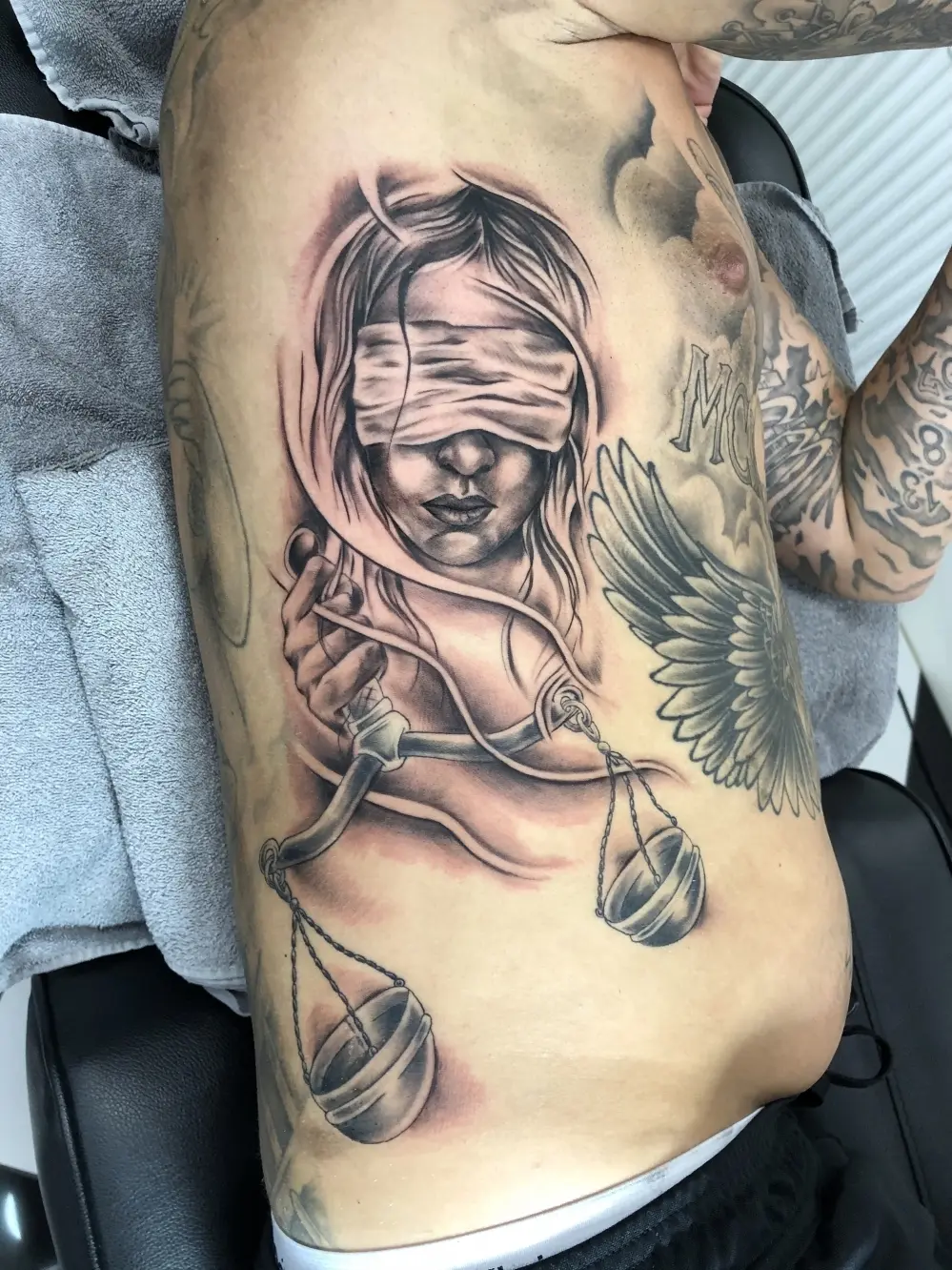 Realistische zwart-wit tattoo van Vrouwe Justitia met weegschaal op de ribben.