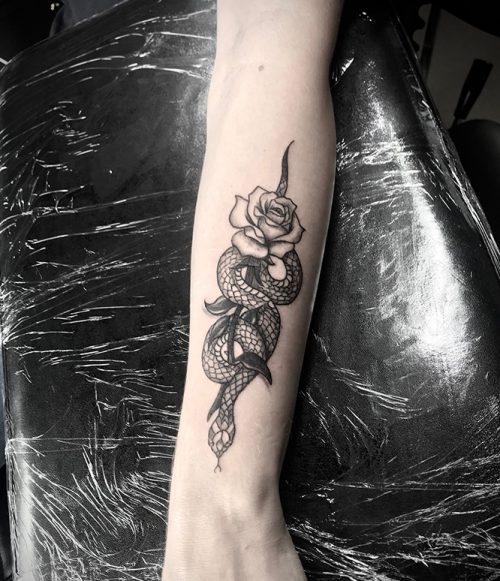 Zwart-wit tattoo van een slang die om een roos kronkelt op de onderarm.
