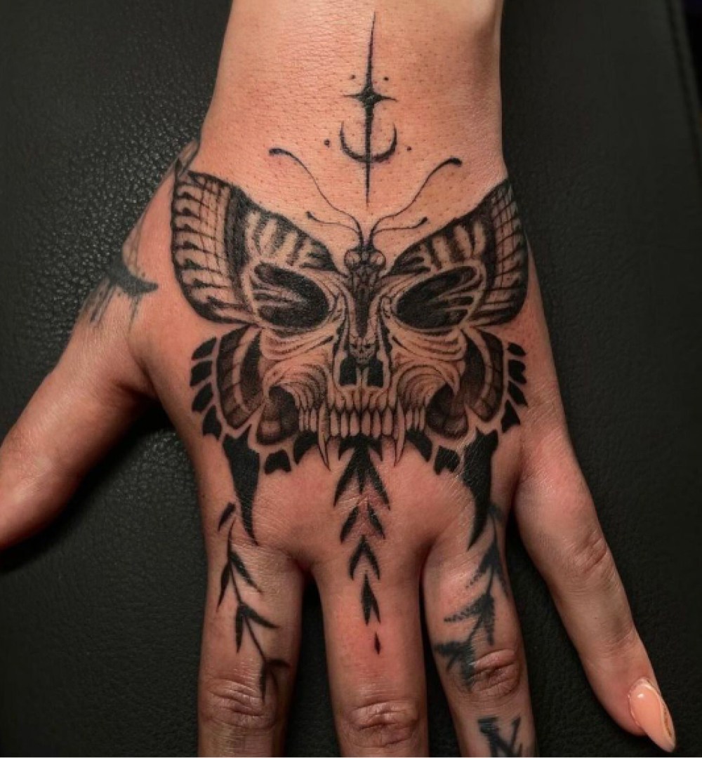 Zwart-wit tattoo van een vlinder met een doodskop op de hand.