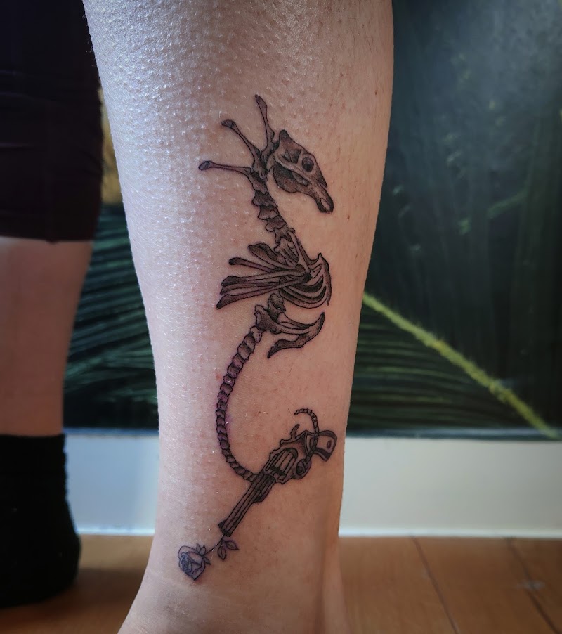 Skelet zeepaardje met revolver en roos op onderbeen.