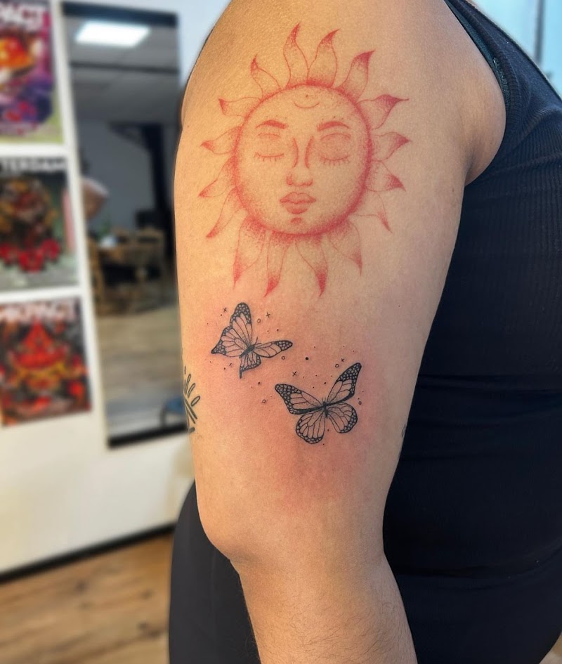 Rode zon met gezicht en twee zwarte vlinders op bovenarm.