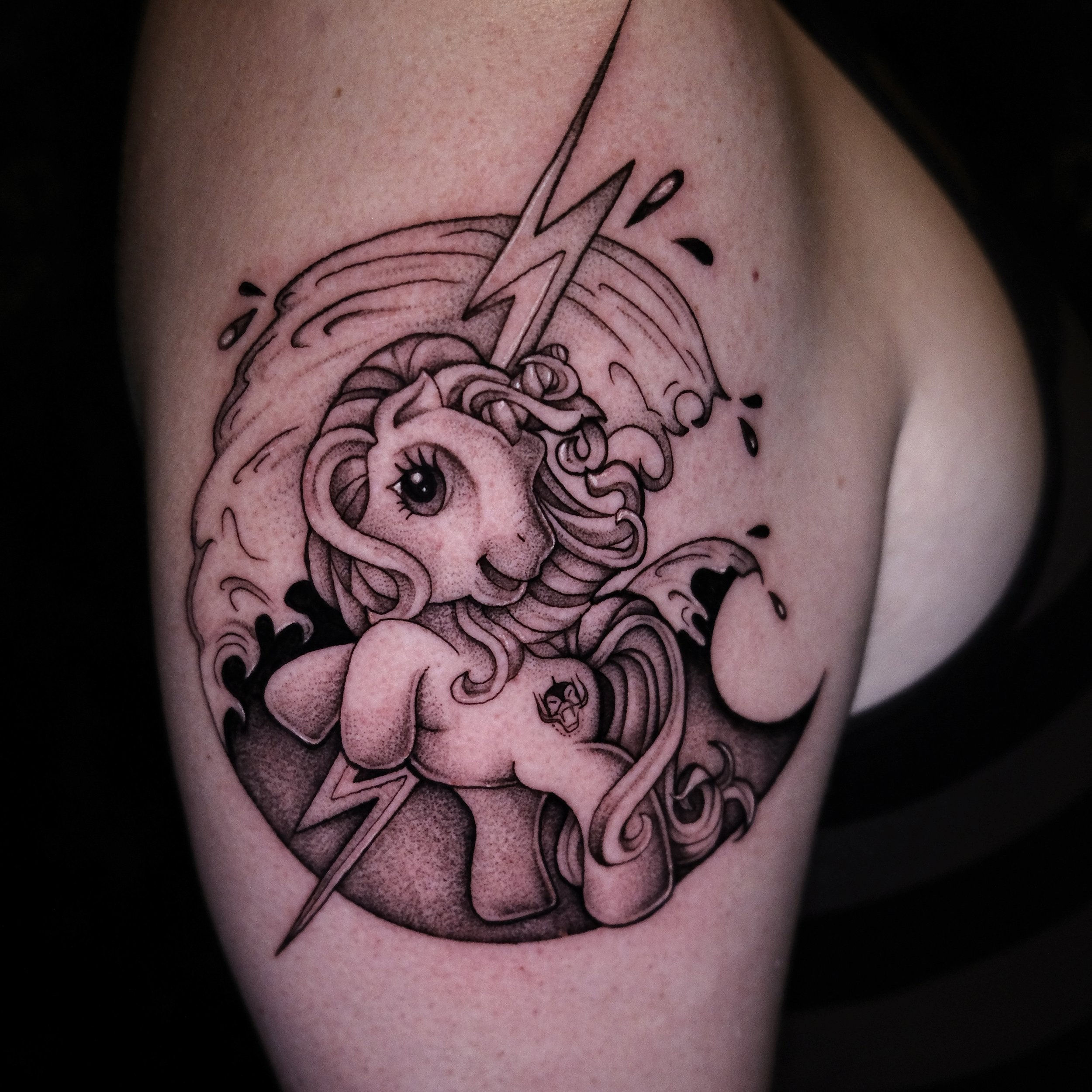 Zwart-wit My Little Pony tattoo met bliksem en golven op bovenarm.