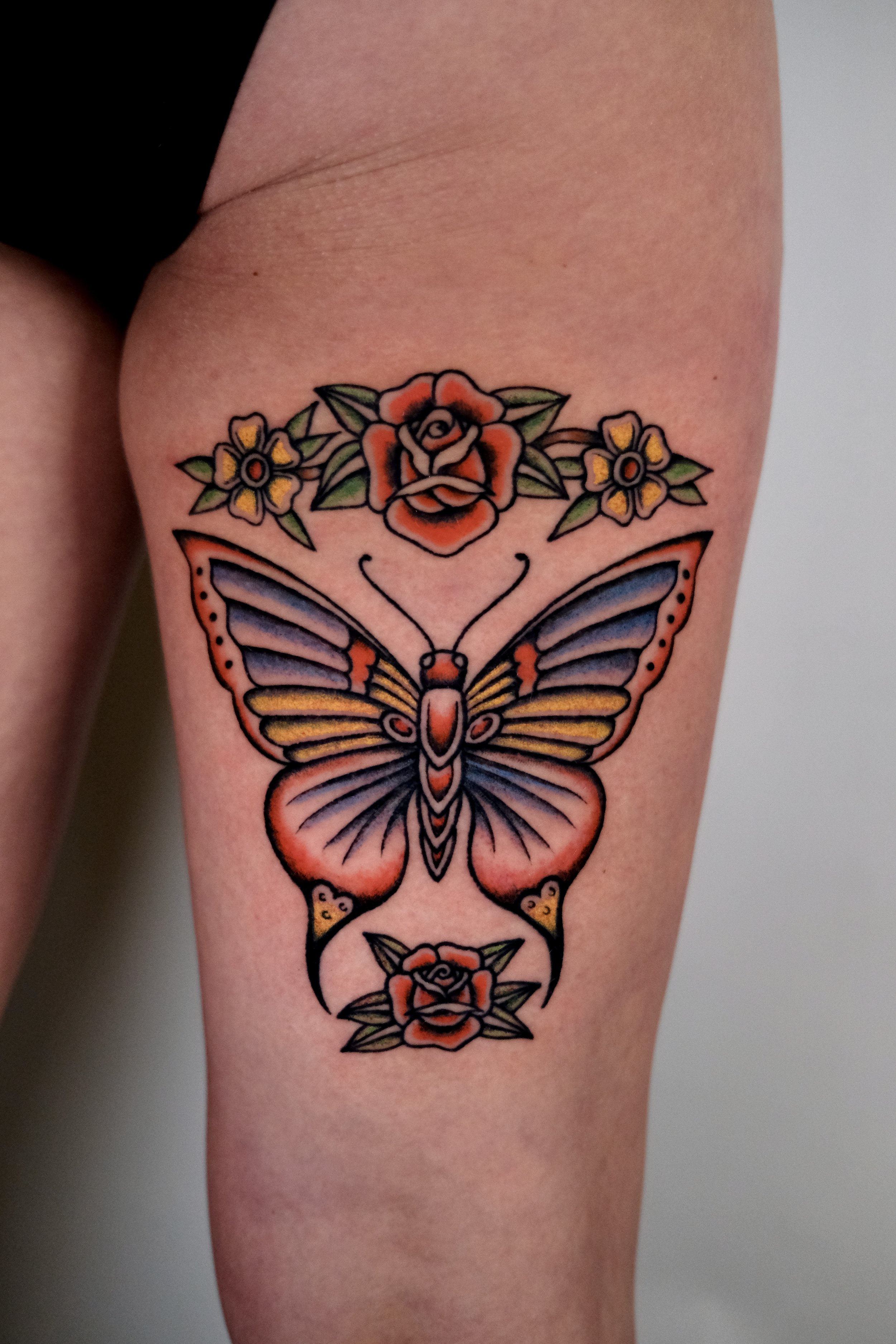 Traditionele vlinder met rozen en bloemen op bovenbeen.