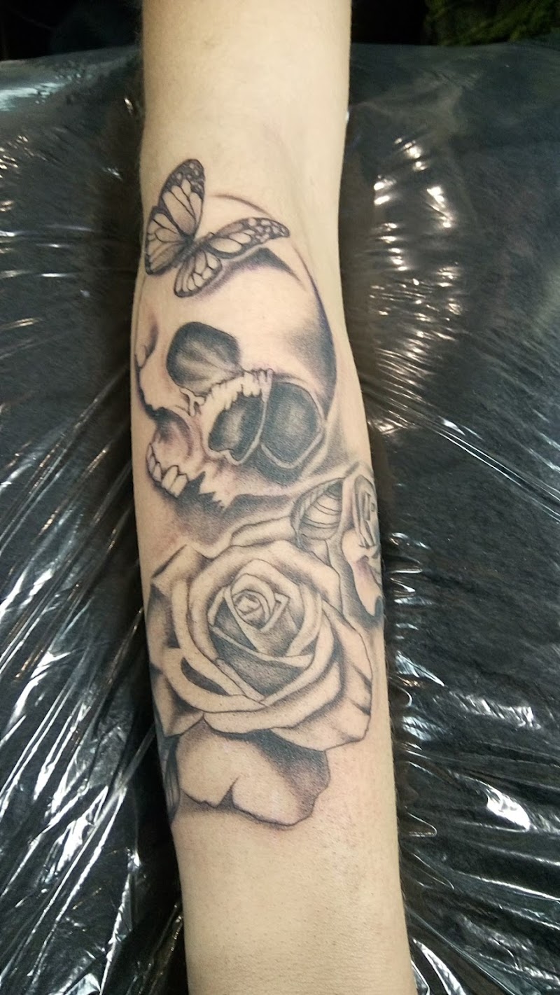 Zwart-wit tattoo van een schedel, roos en vlinder op de onderarm.