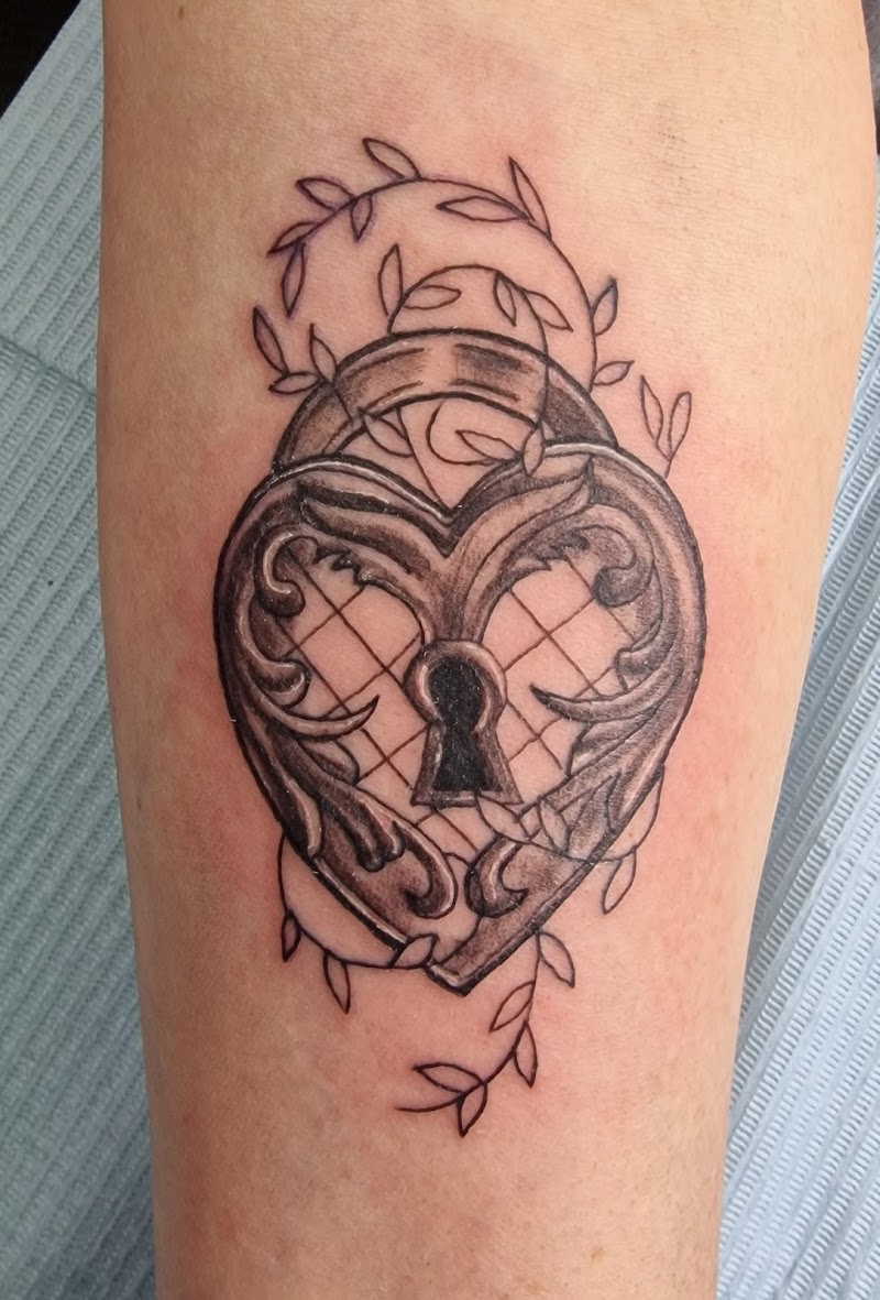 Hartvormig hangslot met sierlijke details en sleutelgat, omringd door bladeren.