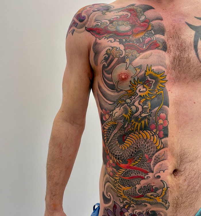 Grote Japanse draak tattoo op de ribben met wolken en golven.