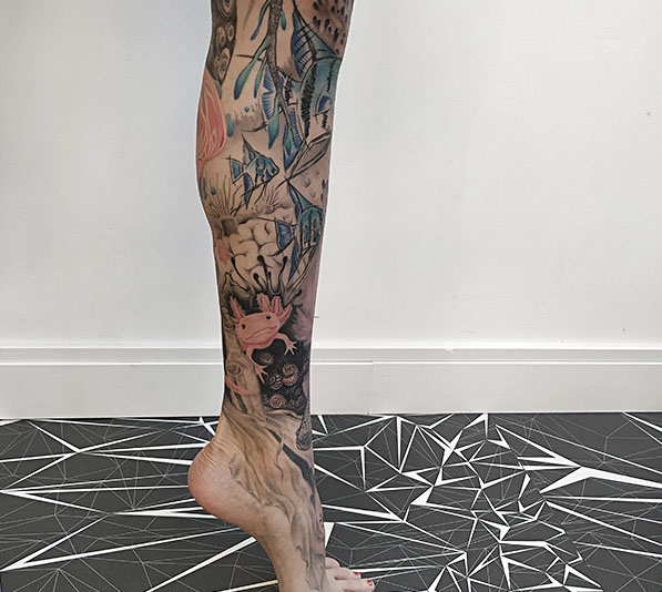 Kleurrijke onderwater tattoo met axolotl en vissen op onderbeen.