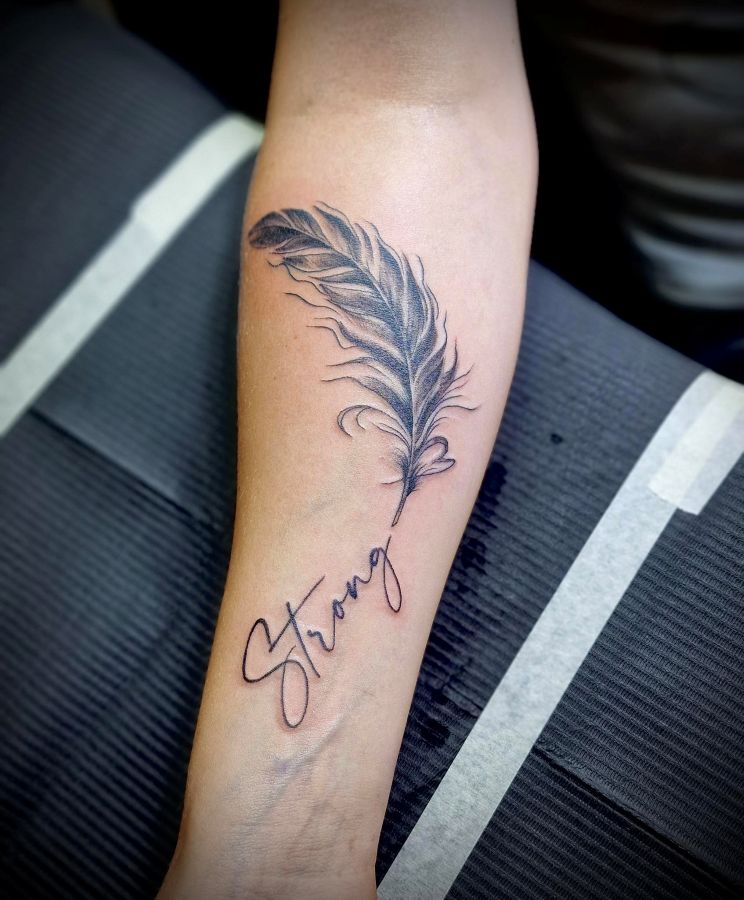 Veer met het woord 'Strong' in sierlijk schrift op de onderarm.