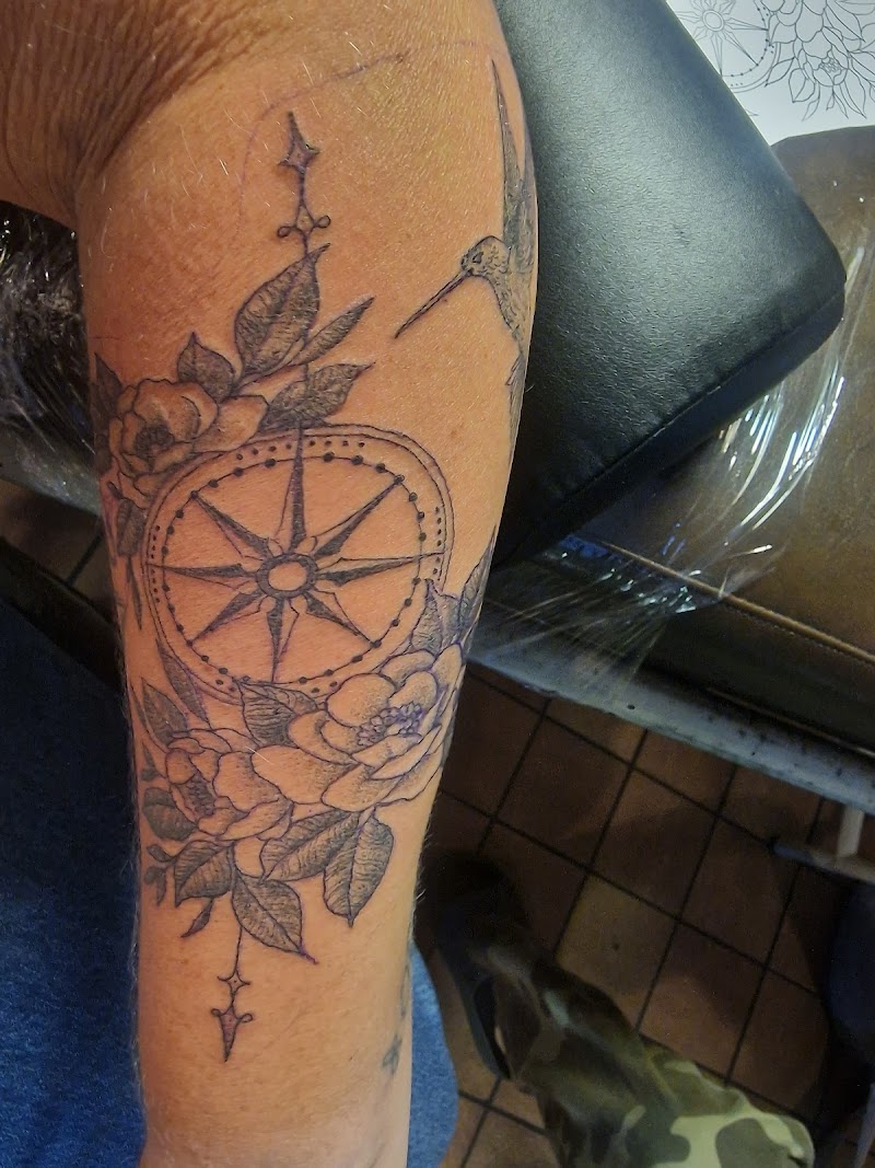 Kompas met bloemen en kolibrie in fineline op onderarm.