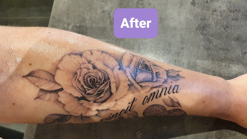 Realistische zwart-wit tattoo van rozen en de tekst 'vincit omnia' op de onderarm.
