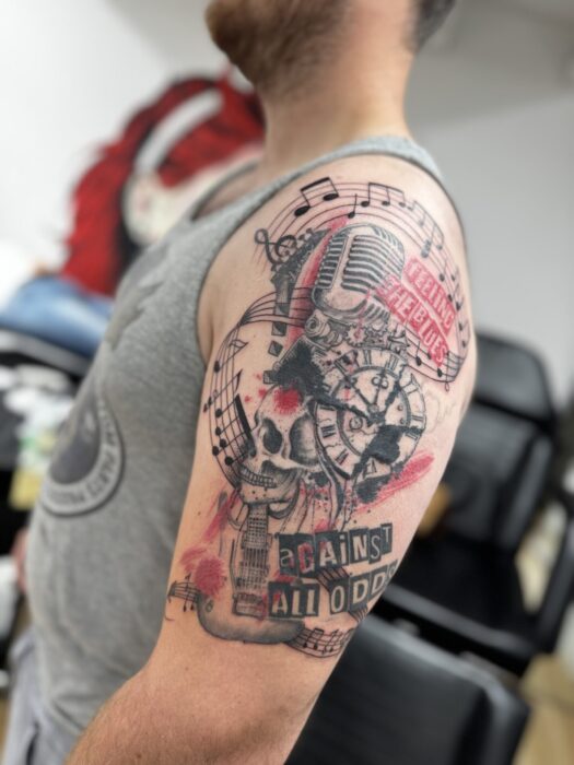 Trash polka tattoo met schedel, microfoon, klok en tekst op bovenarm.