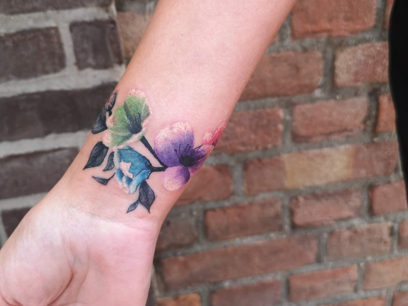 Aquarel bloemenband tattoo op pols.