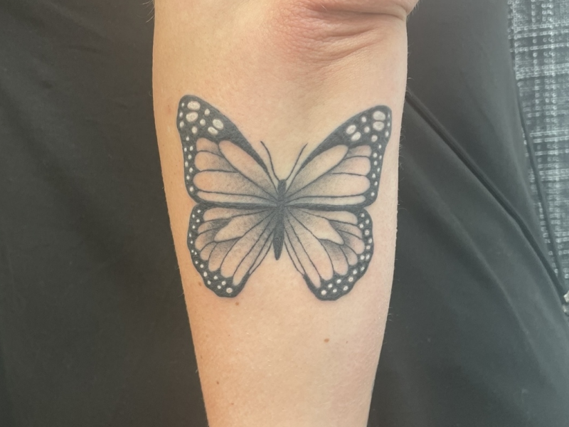 Zwart-witte vlinder tattoo op onderarm.