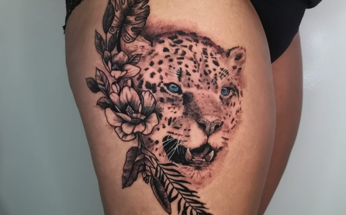 Realistische luipaardkop met blauwe ogen en bloemen op bovenbeen.